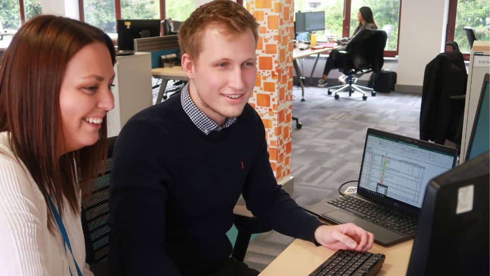 Two accountancy apprentices are looking at a computer screen together at work
