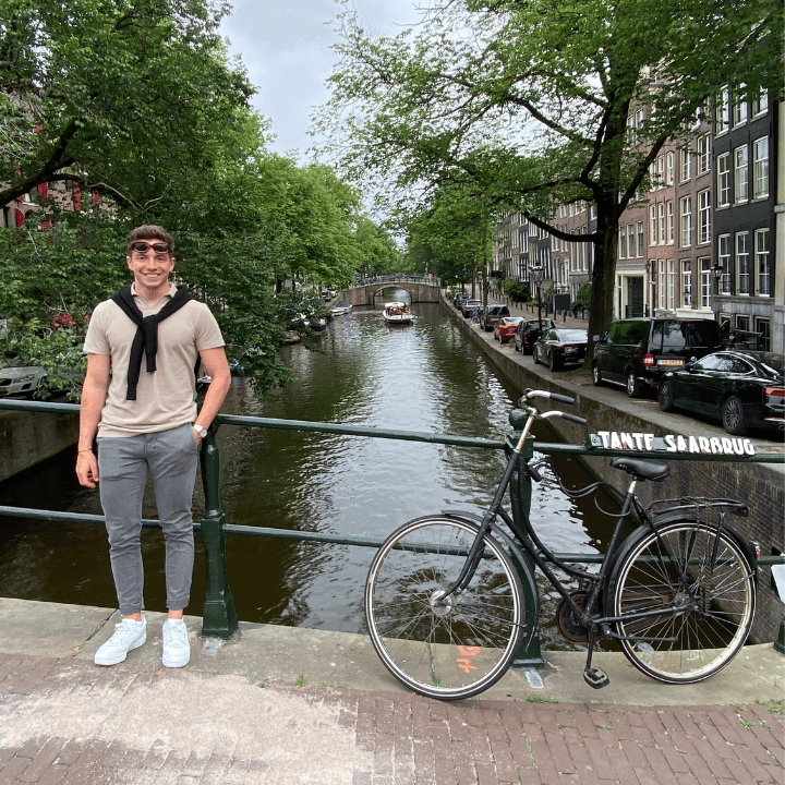 Young professional smiling as he poses for a photo in front of a canal in Amsterdam