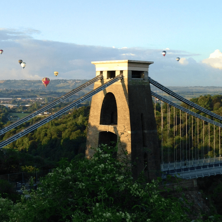 Cifton Suspension Bridge in Bristol on a sunny day with multicoloured hot air balloons flying behind