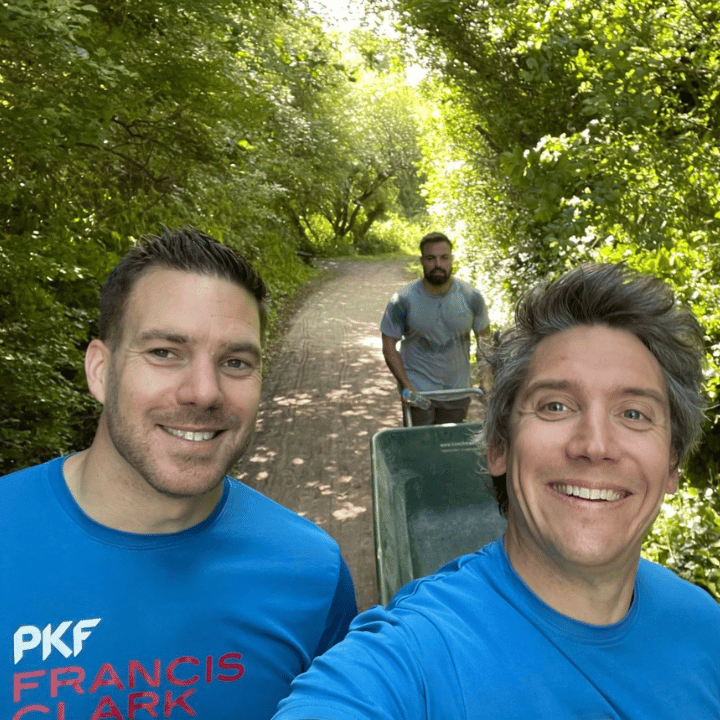 Three colleagues taking a selfie whilst running with one in the background pushing a wheelbarrow