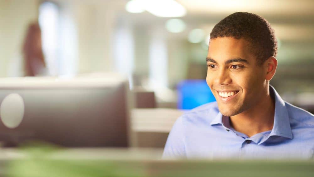Young man smiling as he works on a desktop computer in an office