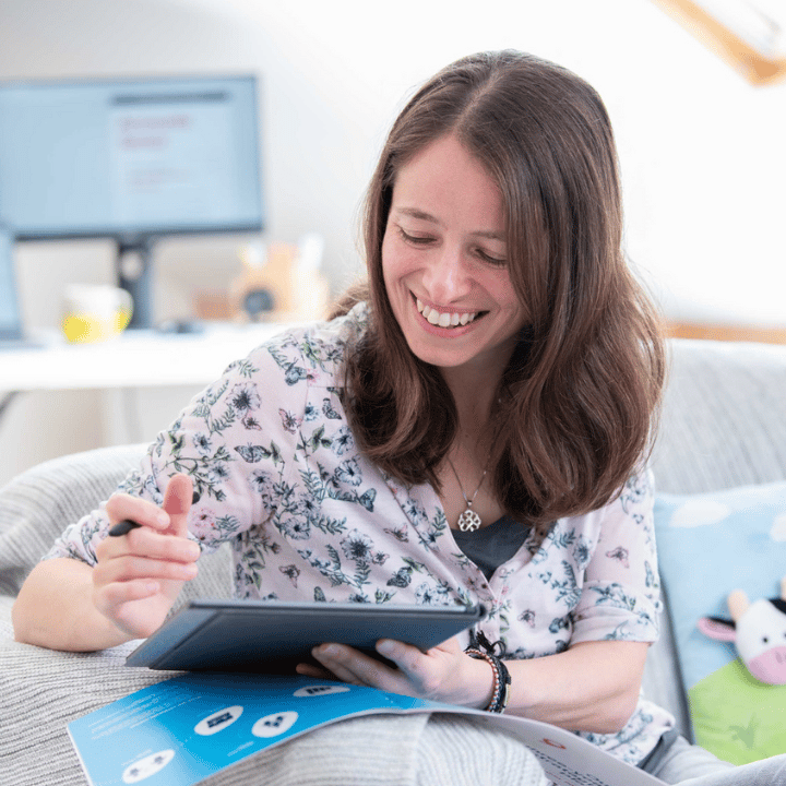 Woman smiling and holding pen in her hand whilst looking at an ipad when working from home