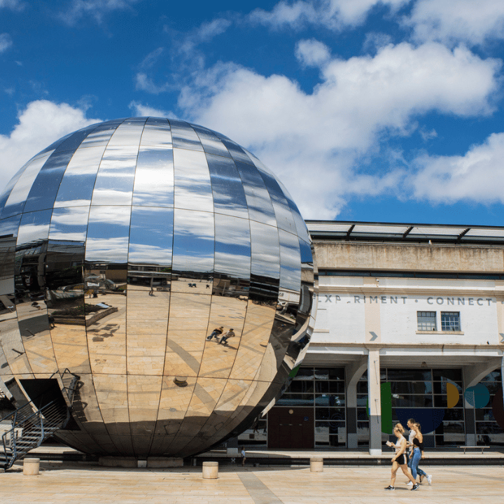 Bristol's Millennium Square on a bright sunny day, with people walking along