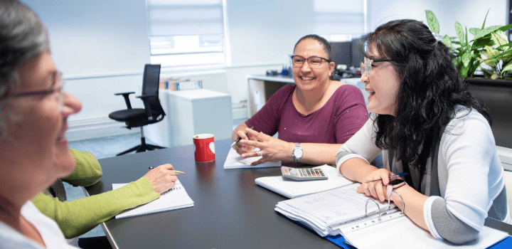 Three women exchange smiles while working together in a break out space