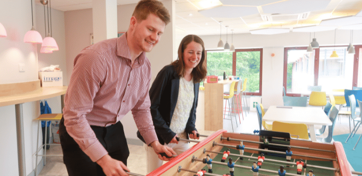 Two team members laughing whilst playing table football in a staff breakout area
