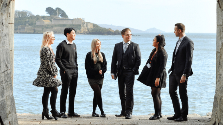 A group of accountants standing outside Royal William Yard with the ocean in the background.