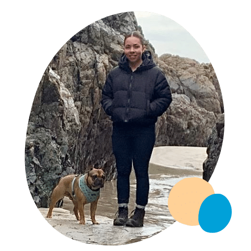 Mollie standing on a beach near some rocks with her dog.