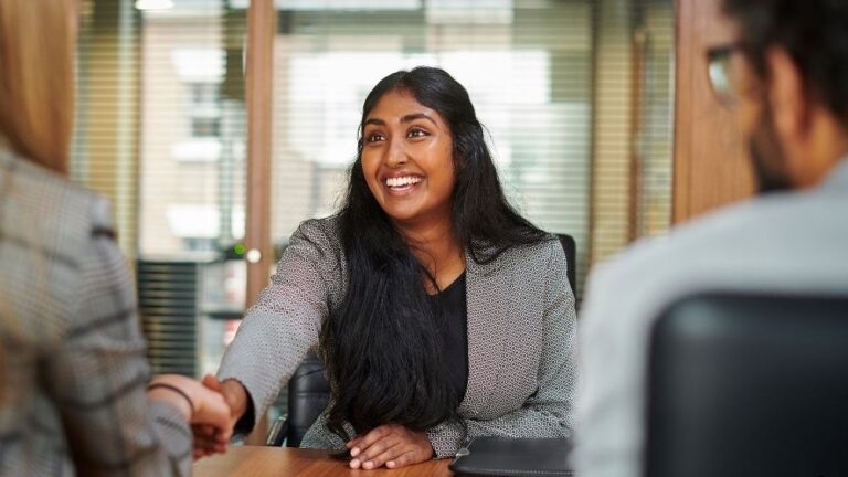 candidate shakes interviewers hand across the desk at an assessment centre